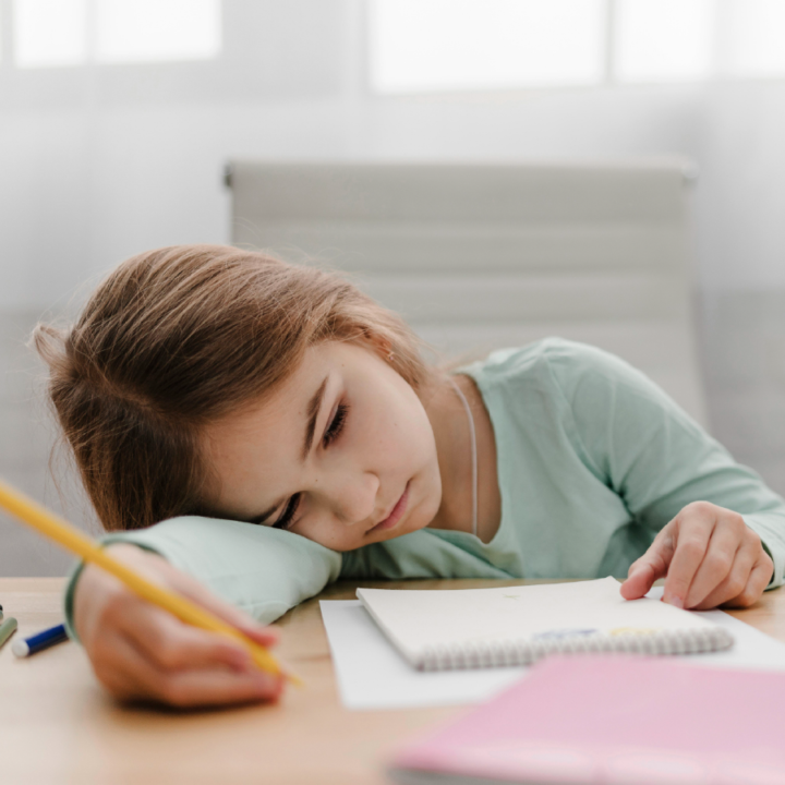 Child with pencil and notebook laying their head on right arm looking bored